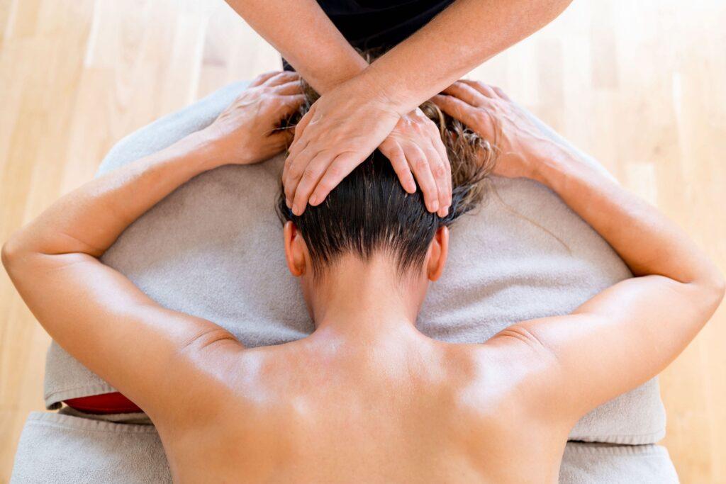 Eine Person, die auf einer gepolsterten Liege eine Nackenmassage im OCÉANO Health Spa Hotel erhält, die Arme entspannt an der Seite. Die Hände des Therapeuten drücken sanft auf den Kopf und schaffen eine beruhigende Atmosphäre.