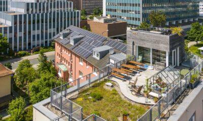 Dachansicht einer Stadtlandschaft mit dem Hotel Luise mit Sonnenkollektoren, üppigem Garten, Sitzbereich und Glasgewächshaus. Moderne, nachhaltige Architektur.