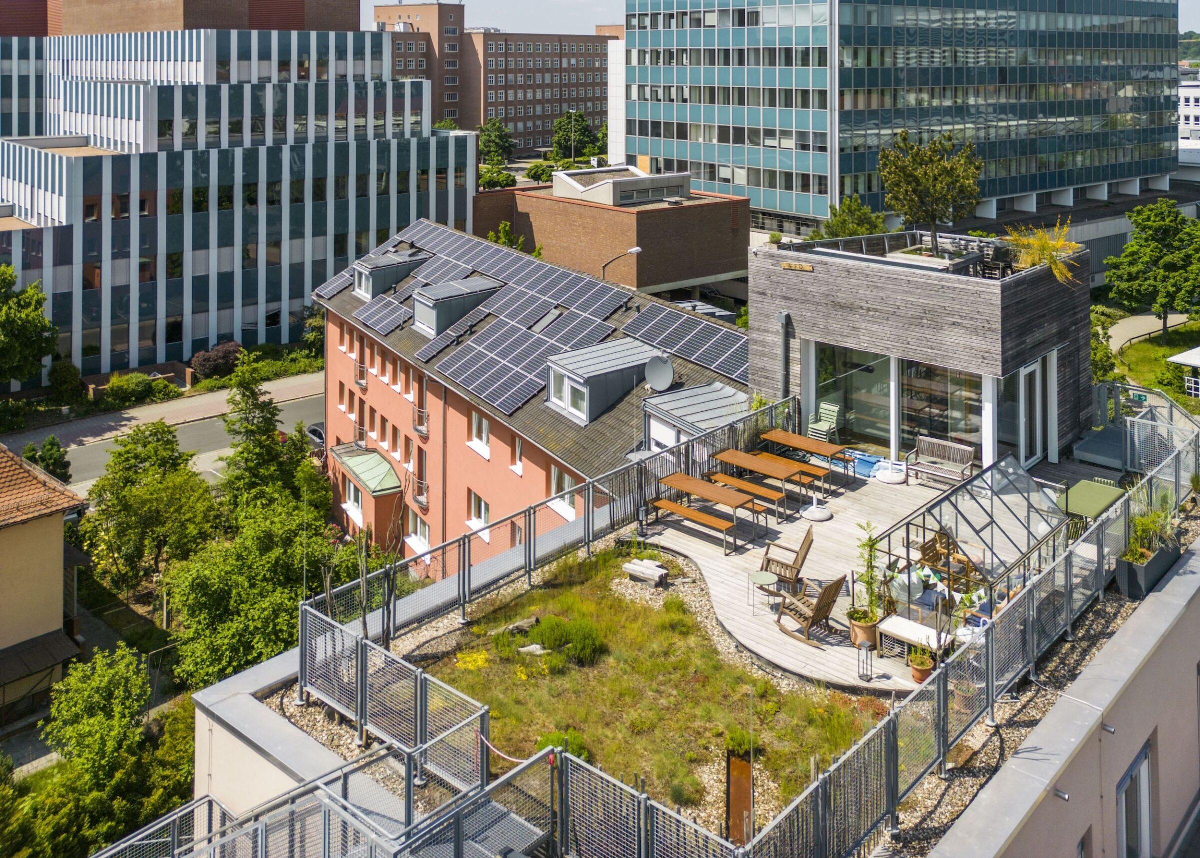 Dachansicht einer Stadtlandschaft mit dem Hotel Luise mit Sonnenkollektoren, üppigem Garten, Sitzbereich und Glasgewächshaus. Moderne, nachhaltige Architektur.