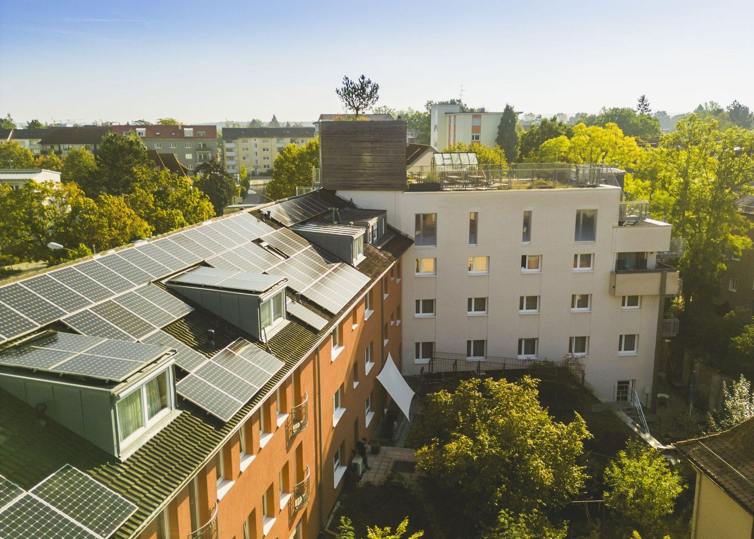 Luftaufnahme des Hotels Luise mit einer großen Anzahl von Solarzellen auf dem Dach, umgeben von Bäumen und anderen Gebäuden an einem klaren, sonnigen Tag.