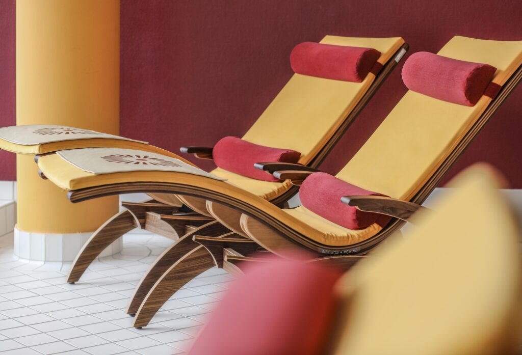 Zwei stilvolle, gelb-rote Lounge-Sessel mit Polsterung stehen vor einer satten, kastanienbraunen Wand und vermitteln ein Gefühl von Entspannung und Luxus in einer eleganten Spa-Umgebung des nachhaltgen Hotels SCHWARZWALD PANORAMA in Bad Herrenalb