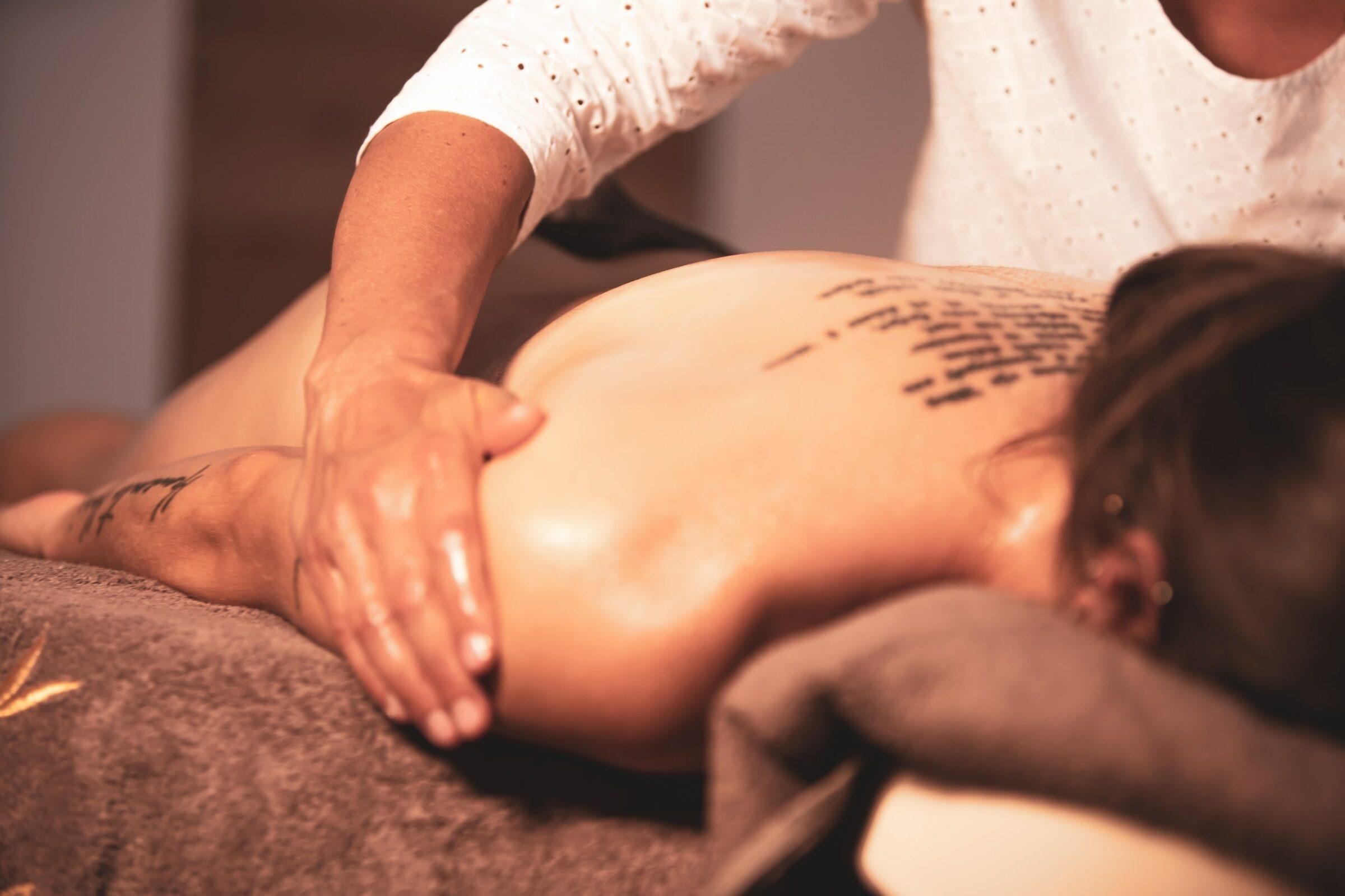 Person, die im veganen Hotel LA VIMEA in Südtirol eine entspannende Rückenmassage erhält, liegend auf einem braunen Handtuch. Der tätowierte Rücken und die entspannte Atmosphäre vermitteln Ruhe und Gelassenheit.