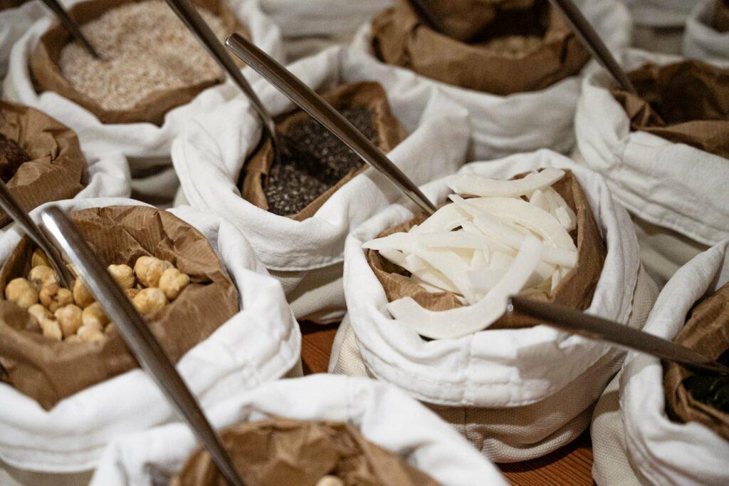Stoffbeutel, gefüllt mit verschiedenen Lebensmitteln wie Nüssen, Chiasamen und Kokosflocken, jeweils mit einer Portionsschaufel, sorgen für eine rustikale Marktatmosphäre beim Frühstücksbuffet des rein veganen Hotels LA VIMEA in Südtirol.