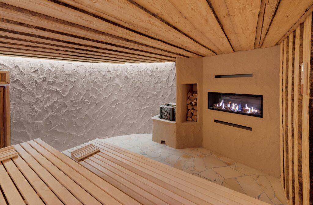 The interior of an earth sauna featuring wooden benches, a wall lined with logs, and a modern fireplace at a sustainable lifestyle resort