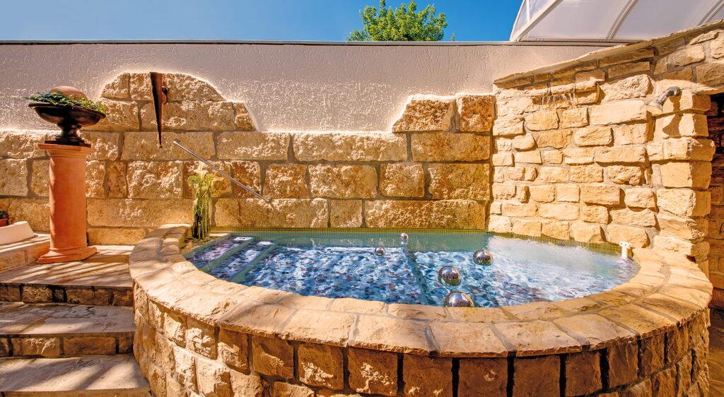 Runder Whirlpool aus Naturstein mit Silberkugeln vor einer Natursteinmauer im Lifestyle Resort Zum Kurfürsten in Bernkastel-Kues