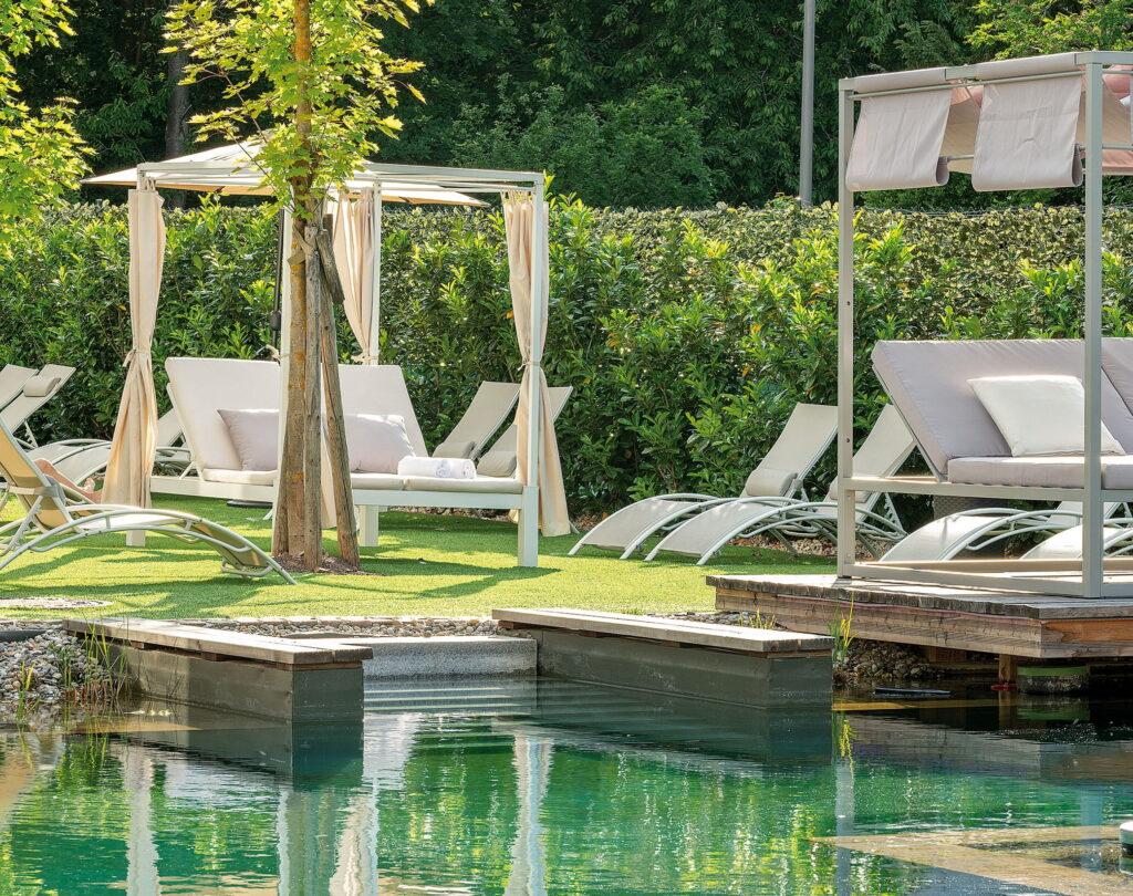 Naturschwimmteich mit Liegen und überdachten Sitzbereichen umgeben von Büschen und Bäumen im Lifestyle Resort Zum Kurfürsten in Bernkastel-Kues