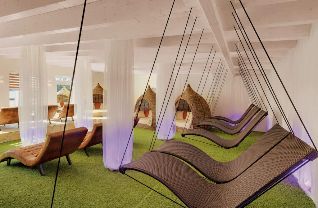 Relaxation room at the Lifestyle Resort Zum Kurfürsten, featuring hanging rattan loungers, seating, and decorative baskets on green carpeting