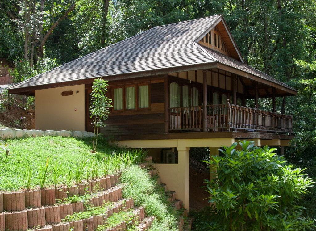 Hölzerne Villa auf Stelzen mit Veranda und Geländer, umgeben von dichtem Grün und terrassiertem Hang im nachhaltigen Cerf Island Resort auf den Seychellen