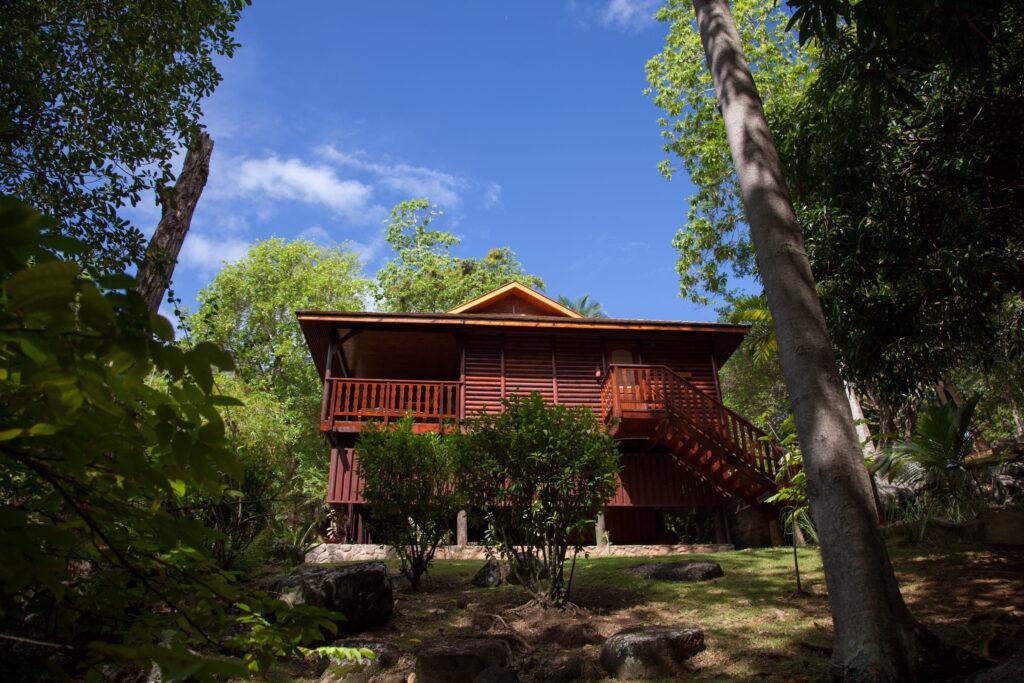Holzvilla im Cerf island Resort auf Stelzen mit Veranda und Außentreppe umgeben von tropischer Vegetation der Seychellen unter blauem Himmel
