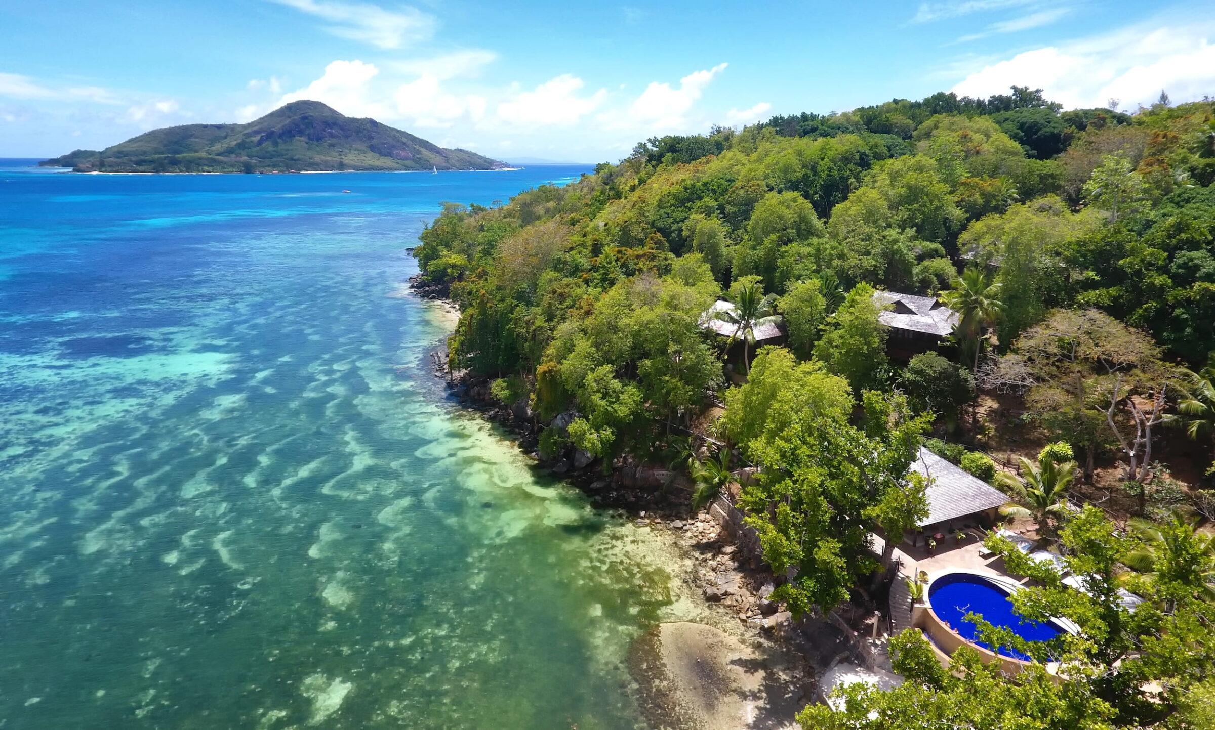 Luftaufnahme des nachhaltigen Cerf Island Resorts auf den Seychellen mit grüner Vegetation, mehreren Gebäuden und einem Pool am Ufer des türkisfarbenen Meeres