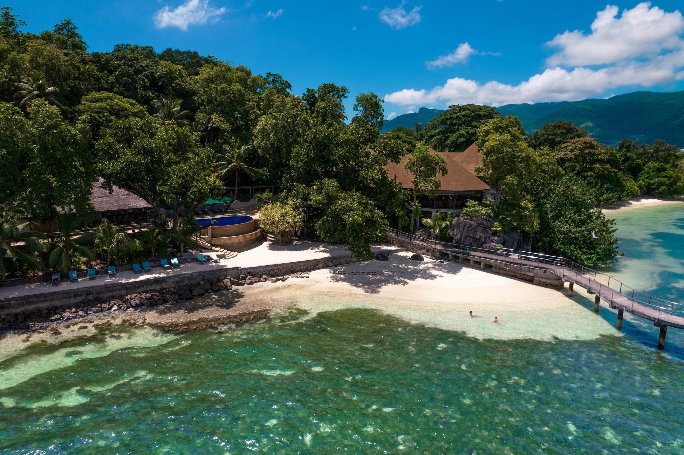 Nachhaltiges Cerf Island Resort auf den Seychellen mit kleinen Stränden, umgeben von dichtem Grün und klarem Wasser, mit Steg und einzelnen Personen im Wasser