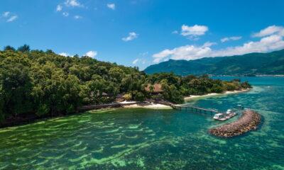 Holzsteg führt von einem bewaldeten Strandabschnitt des Cerf Island Resorts auf den Seychellen zu einem kleinen Bootsanleger im türkisfarbenen Meer