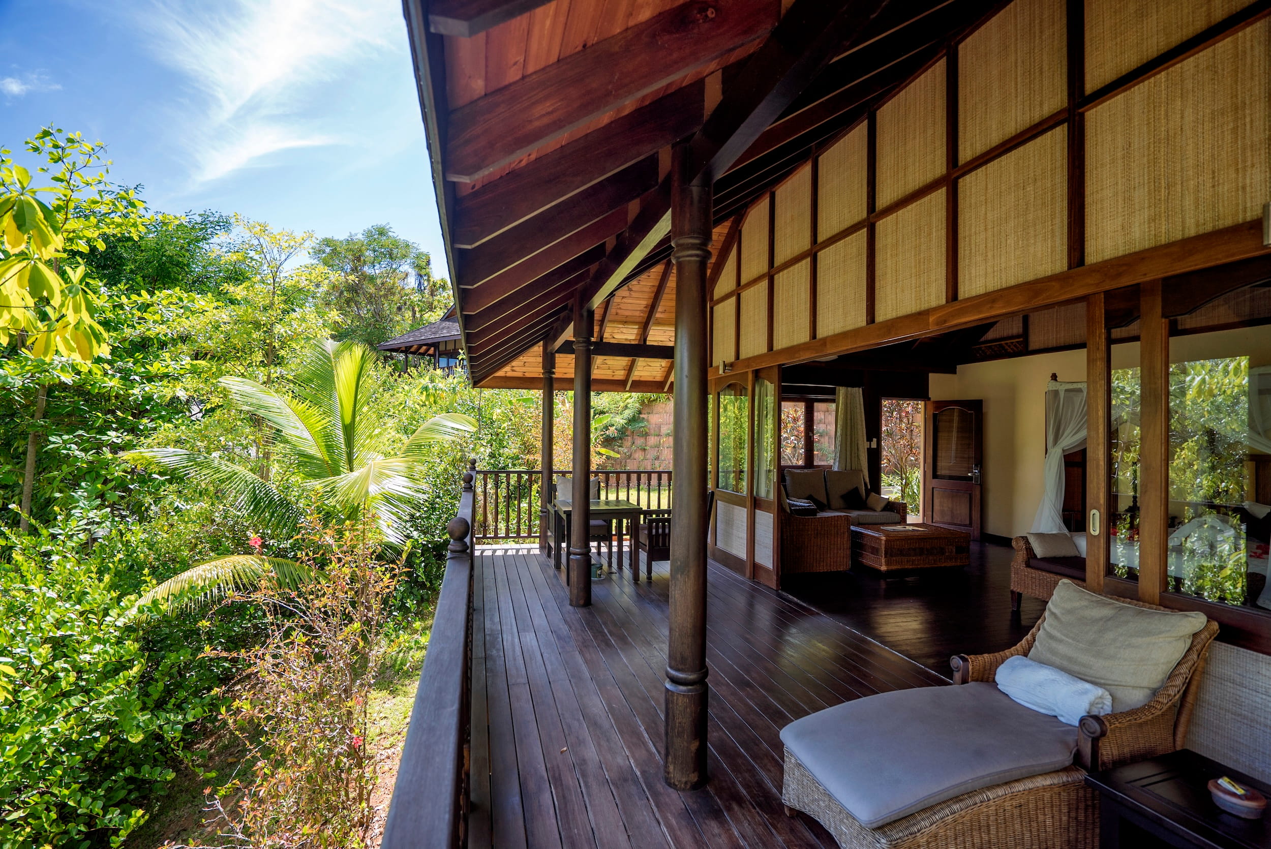 Offene Veranda einer Villa im nachhaltigen Resort auf Cerf Island mit Holzboden, Säulen, Rattanmöbeln und Blick auf tropische Vegetation