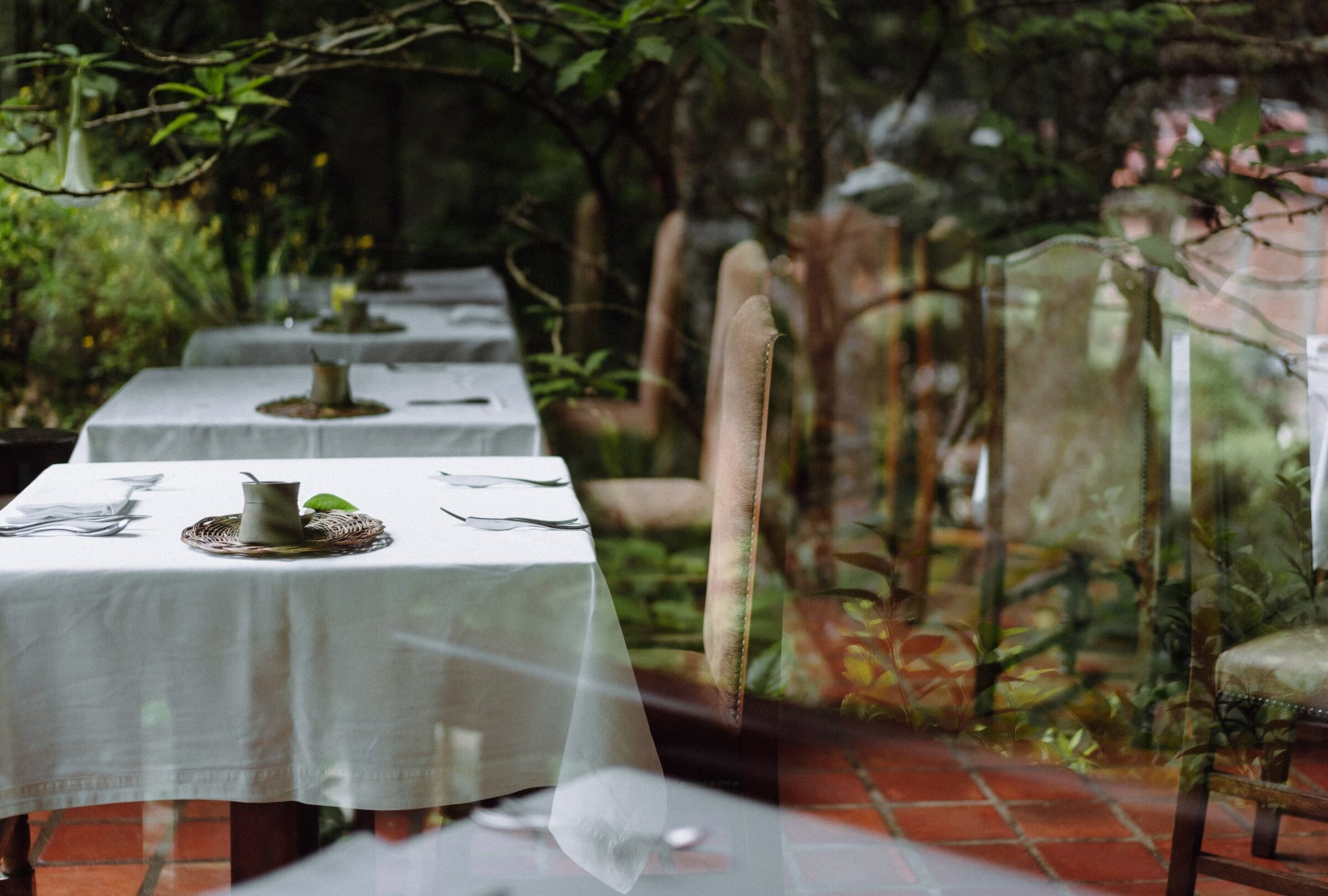 Das elegante Restaurant des Inkaterra Machu Picchu Pueblo Hotels in Peru mit Tischen, die mit weißen Tischdecken gedeckt sind, liegt eingebettet in üppigem Grün und spiegelt Pflanzen auf Glas wider, wodurch eine ruhige, einladende Atmosphäre entsteht.