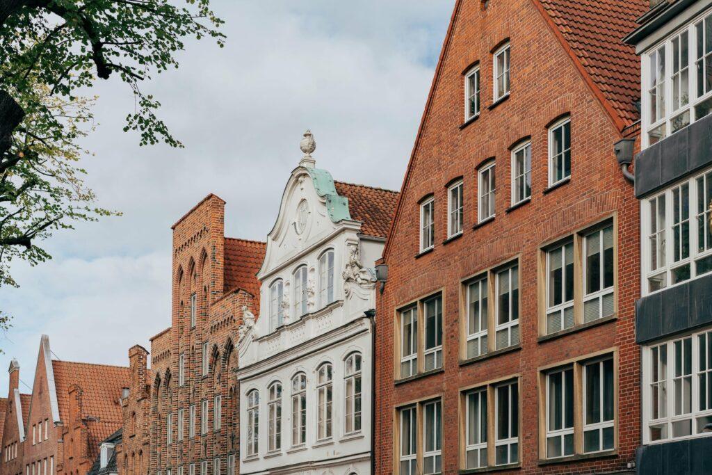 Historische europäische Straße in Lübeck mit roten Backsteinen und verzierten weißen Gebäuden, Spitzdächern und hohen Fenstern unter einem teilweise bewölkten Himmel. Friedlich und zeitlos.
