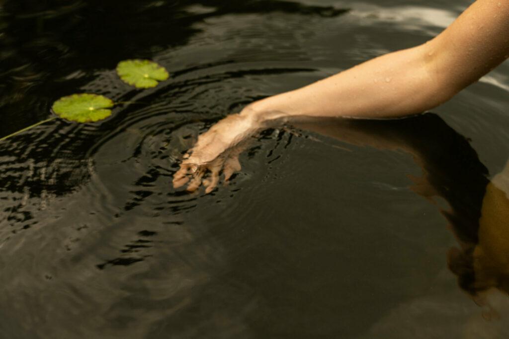 Naturteich mit Hand im Wasser im nachhaltigen Hotel STURM in der Rhön