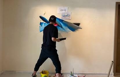 Eine Person in legerer schwarzer Kleidung schafft abstrakte blaue Kunst an einer Wand, umgeben von Werkzeugen und Farbe, im veganen Hotel Paradiso Pure.Living. Die Szene vermittelt Kreativität und Konzentration.