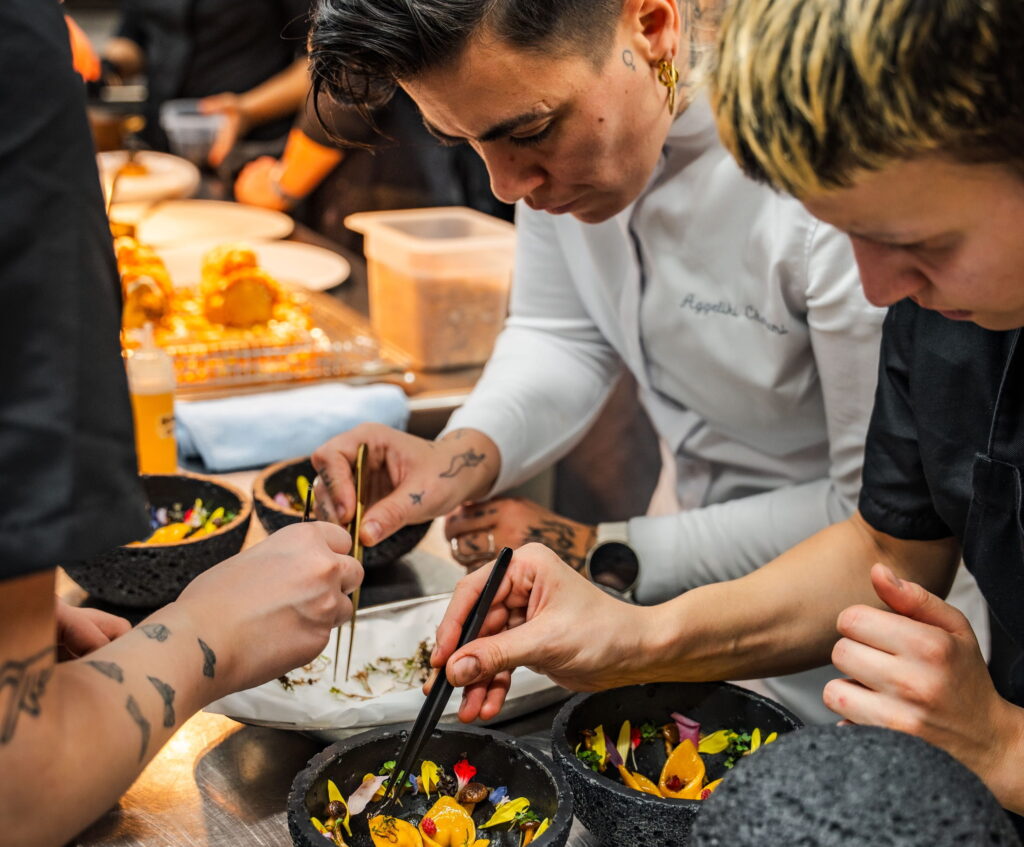 Vegane Köche konzentrieren sich in einer geschäftigen Küche intensiv darauf, mit Pinzetten farbenfrohe Gerichte anzurichten, und vermitteln dabei Präzision und Kreativität. Die Szene stammt aus dem Vegan Fine Dining Restaurant OMNIA vom Paradiso Pure.Living in Südtirol.