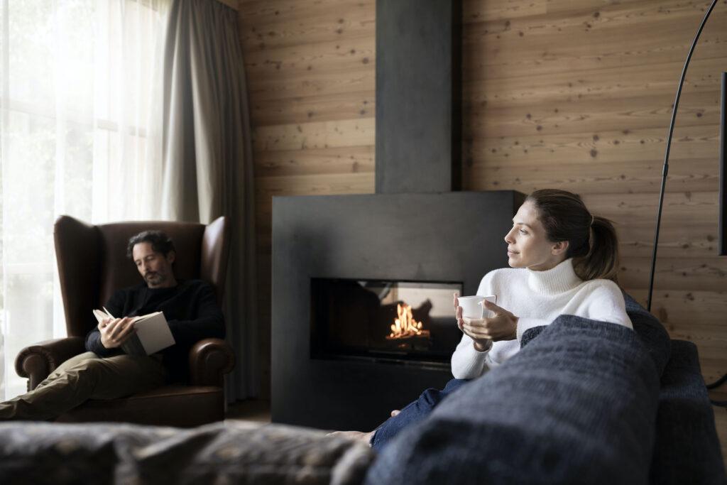 Pärchen sitzt im Wohnzimmer ihres nachhaltigen Privatchalets in der ADLER Lodge RITTEN am Kamin