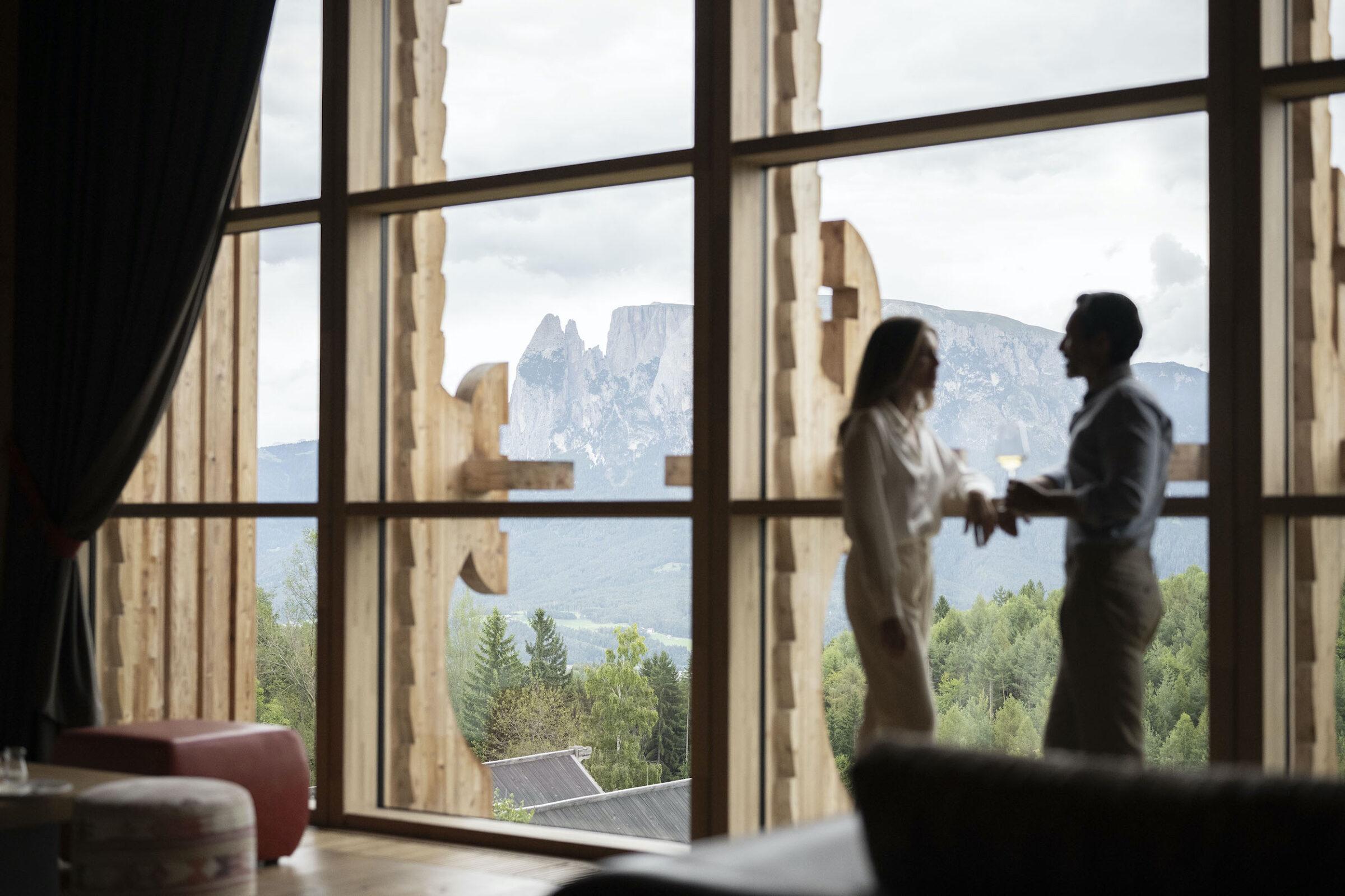 Paar steht vor dem Panoramafenster mit Bergblick im nachhaltigen Luxushotel ADLER Lodge RITTEN in Südtirol