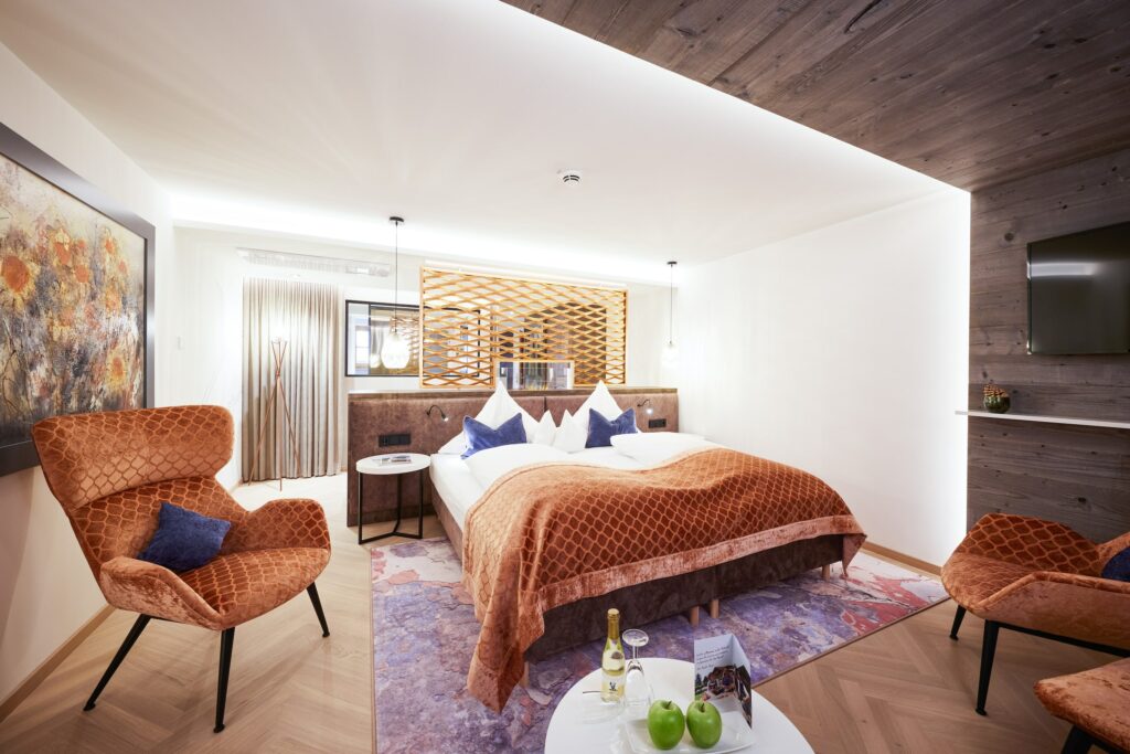 Moderne Hotelsuite im Boutique Hotel Das Rübezahl in Bayern mit gemütlicher Atmosphäre, ausgestattet mit einem weichen Bett mit kupferfarbener Bettwäsche, eleganten Sesseln, abstrakter Kunst, sanfter Beleuchtung und dekorativen Akzenten in Kupfer und Blau.