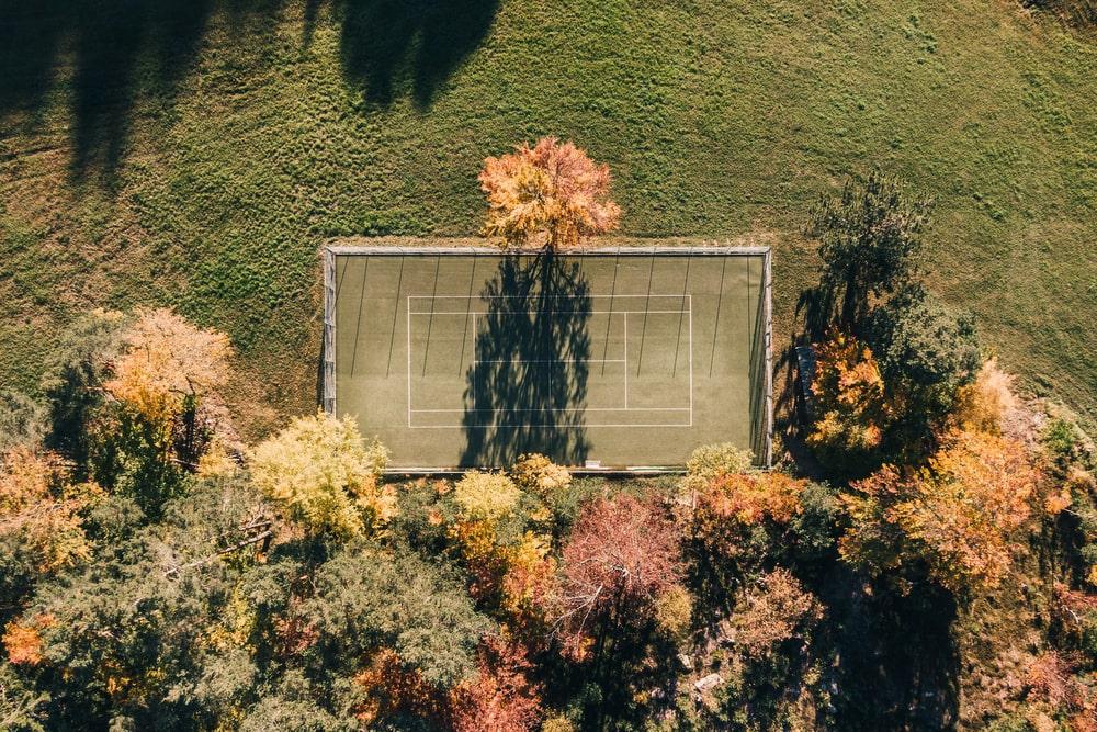 Luftaufnahme des Tennisplatzes des Hotel Weihrerhofs, umgeben von leuchtenden Herbstbäumen, die lange Schatten werfen. Die Szene vermittelt eine ruhige und friedliche Atmosphäre.