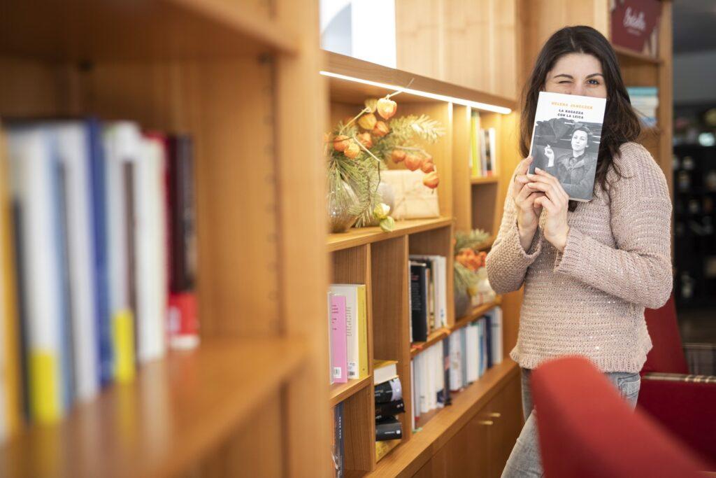 Eine Frau, die spielerisch ein Buch vor ihr Gesicht hält, zwinkert in der gemütlichen