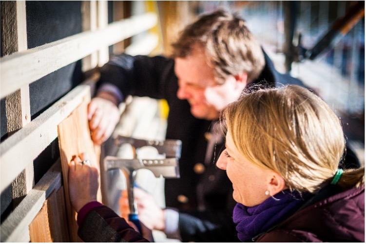 The owners and hosts of the sustainable Klosterhof – Alpine Hideaway & Spa hotel in southern Bavaria are working on the hotel, focusing on installing traditional larch shingles on the façade. They look busy and focused, tools in hand.