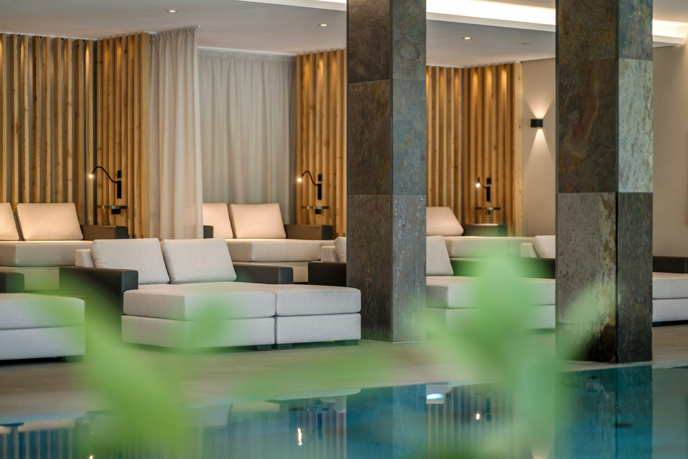Modern spa relaxation area with light brown deckchairs, soft lighting and wooden slat accents at the sustainable wellness hotel Klosterhof – Alpine Hideaway & Spa in Bavaria. A calm interior design with a soothing ambiance.