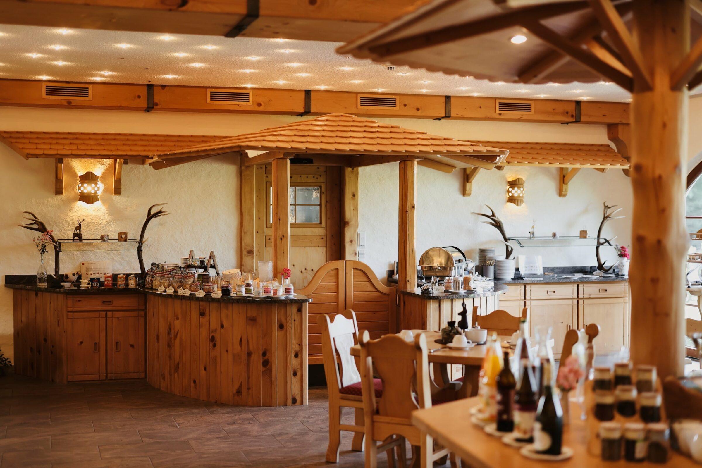 Rustikales Frühstücksbuffet im Naturresort Gerbehof am Bodensee mit Holzdekor, Akzenten aus Geweihen und sanfter Beleuchtung. Die Tische sind mit Gläsern und Gewürzen gedeckt, was eine gemütliche, einladende Atmosphäre schafft.