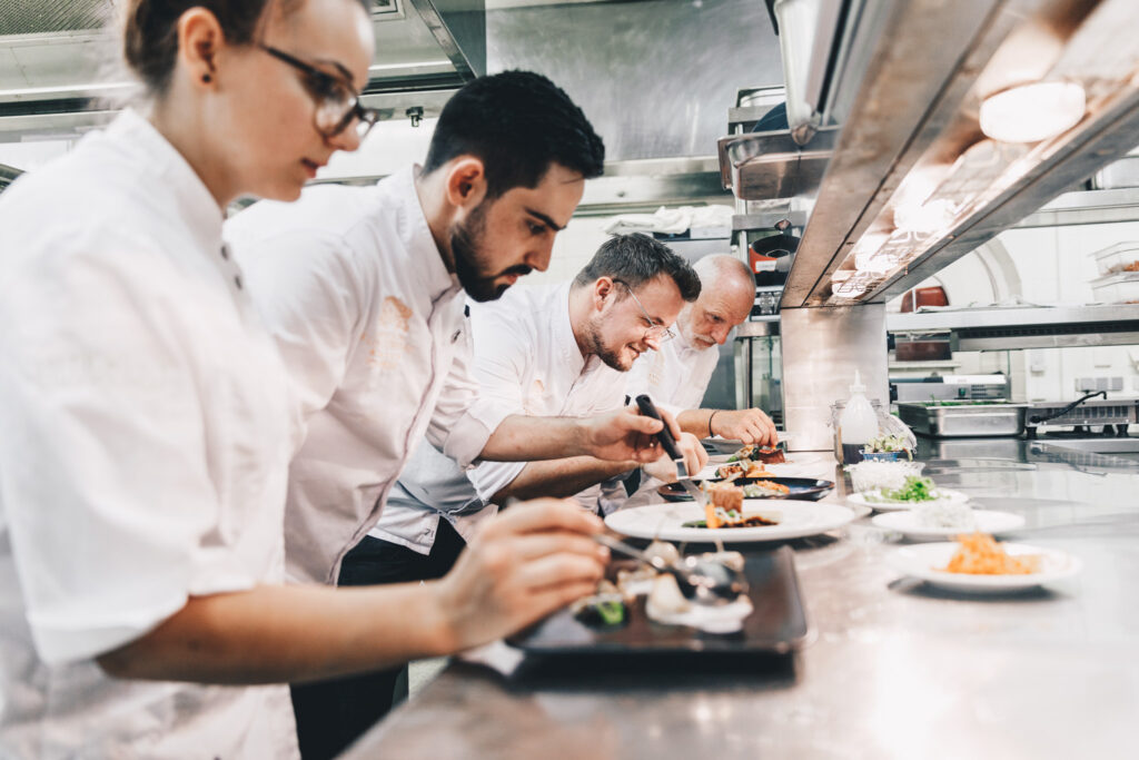 Es wird angerichtet: Blick in die Küche, in der vier Köche jeweils einen Dinner-Teller anrichten