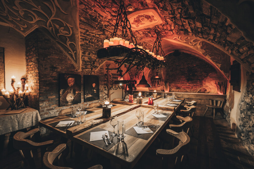 Zu sehen ist eine der neun Dinnerlocations: Hier unter einem steinernen Gewölbe des Klosters mit zahlreichen Kerzen auf einem schwebenden Leuchter