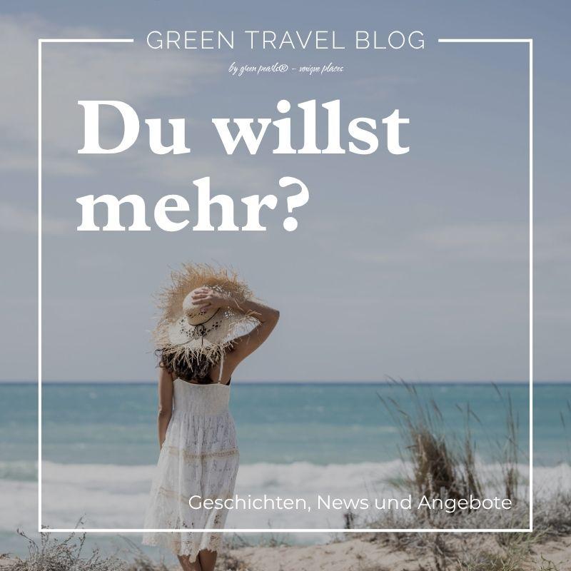Frau im weißen Kleid und Strohhut steht am Strand und blickt aufs Meer
