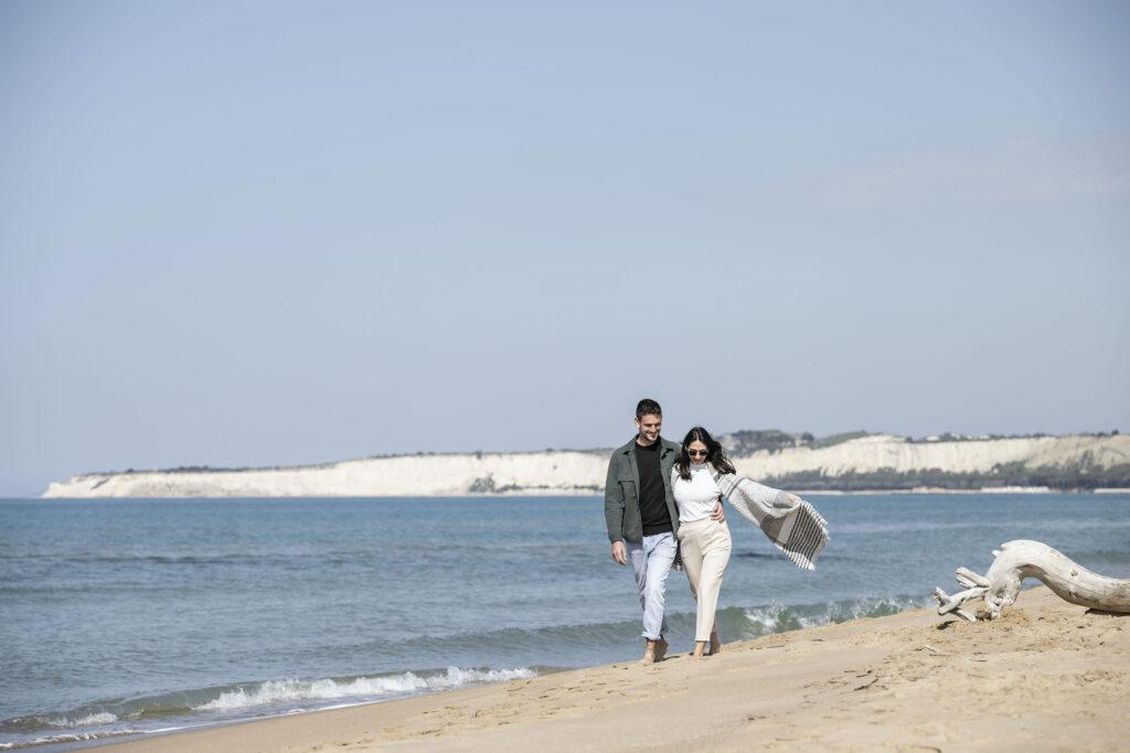 Two people walk along the beach in front of the sustainable ADLER Spa Resort SICILIA in winter