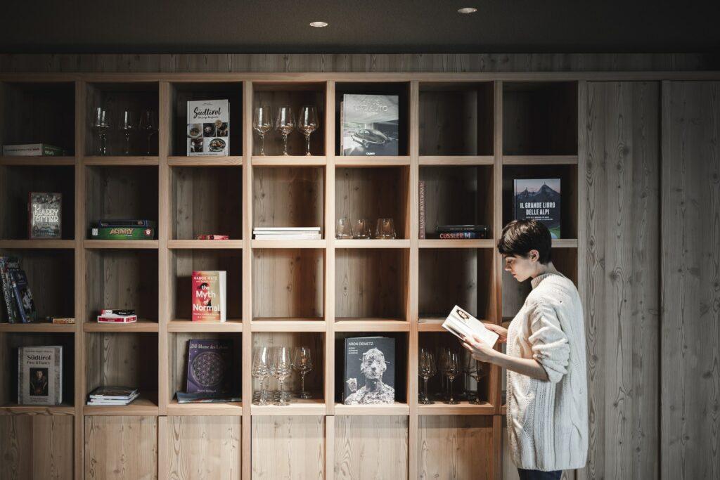 A young woman stands in front of a minimalist wooden shelving unit. OLM Nature Escape in South Tyrol.