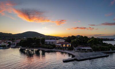 Hotel Korinjak an der kroatischen Küste bei Sonnenuntergang mit ruhigem Wasser, bewaldeten Hügeln und Gebäuden am Ufer