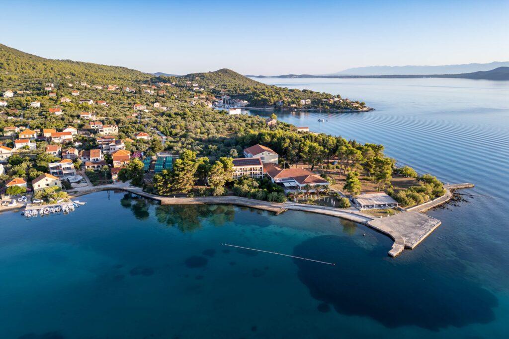 Luftaufnahme des vegetarischen Hotels Korinjak in Kroatien mit umliegendem Dorf, bewaldeten Hügeln und ruhiger Meeresbucht