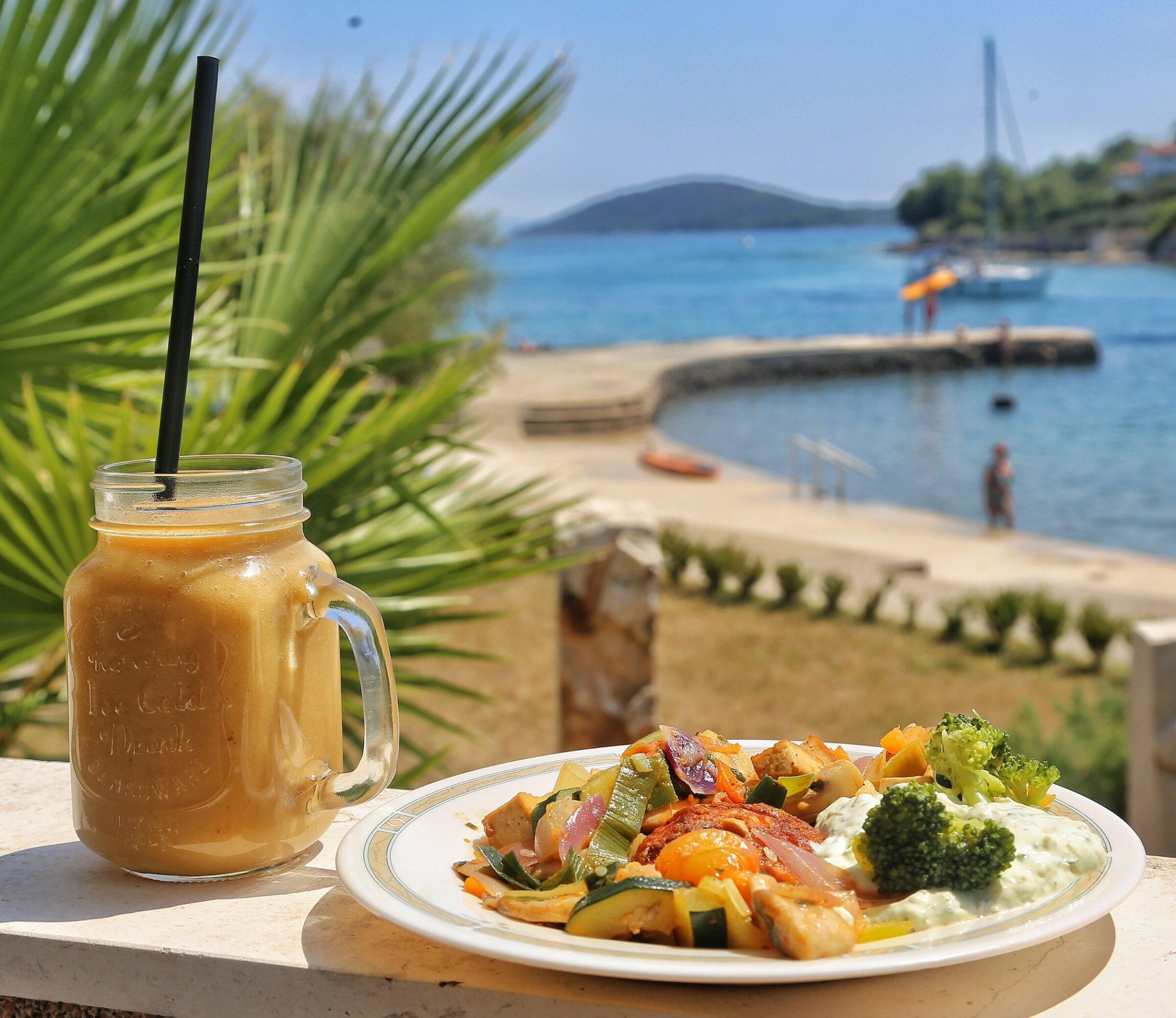 A refreshing smoothie and a plate of colorful grilled vegetables with tzatziki from the vegetarian hotel Korinjak, located on a wall overlooking the sunny sea of the Croatian island of Iz