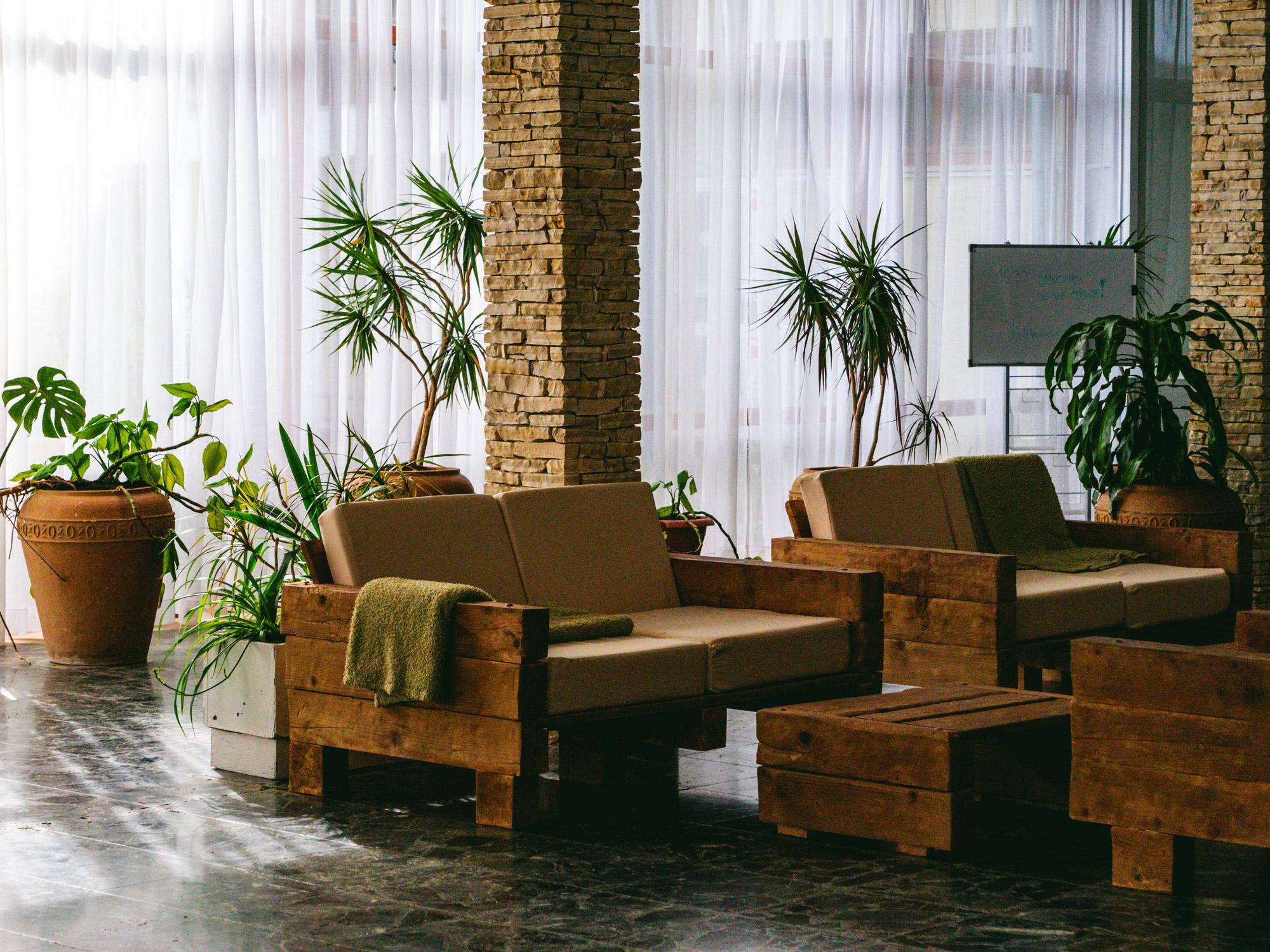 The spacious lobby of the sustainable Hotel Korinjak features stone columns, white curtains, wooden sofas and potted plants, creating a calm, natural atmosphere with warm, earthy tones.