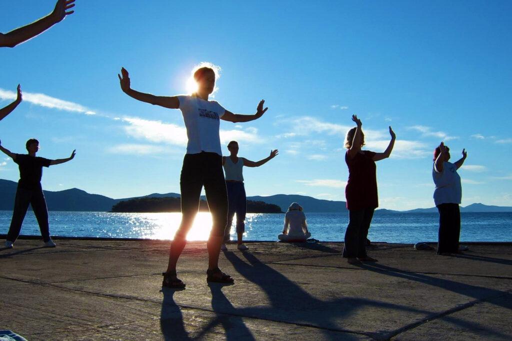 Menschen, die bei Sonnenaufgang im Hotel Korinjak am Meer Tai Chi praktizieren, werfen lange Schatten auf den Boden und schaffen eine ruhige und friedliche Atmosphäre.