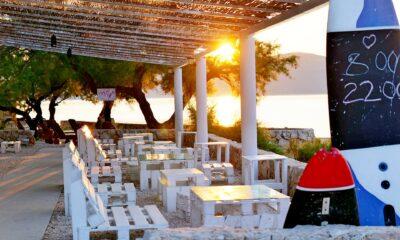Sunset view of the café at the sustainable Hotel Korinjak with white pallet furniture and a pergola. Sunlight filters through the trees at the water's edge, creating a serene atmosphere.