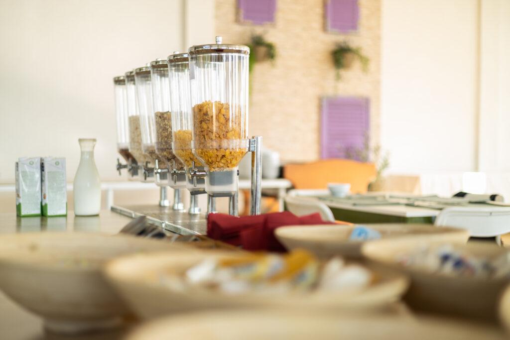 Vegetarisches Frühstücksbuffet im Hotel Korinjak mit Müslispendern und Milch auf einer Theke. Schüsseln im Vordergrund. Helle, gemütliche Umgebung mit einer entspannten Atmosphäre.