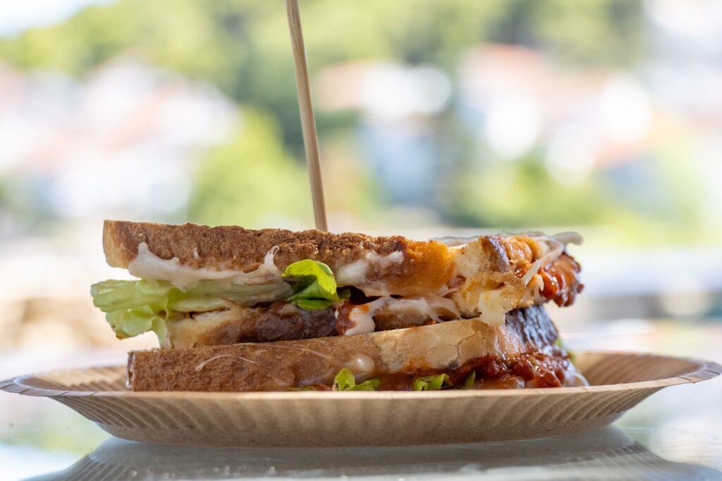 Vegetarisches Sandwich mit Salat, Käse und Soße auf Vollkornbrot auf einem Papierteller mit Holzspieß
