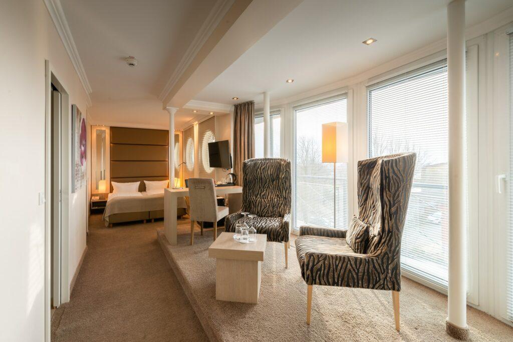 Elegant hotel room at the SANDglow eco-hotel in Husum, reserved for adults only, with zebra-patterned chairs and a small table in a bright seating area. Large bed and TV in the adjoining room. Quiet, luxurious atmosphere.