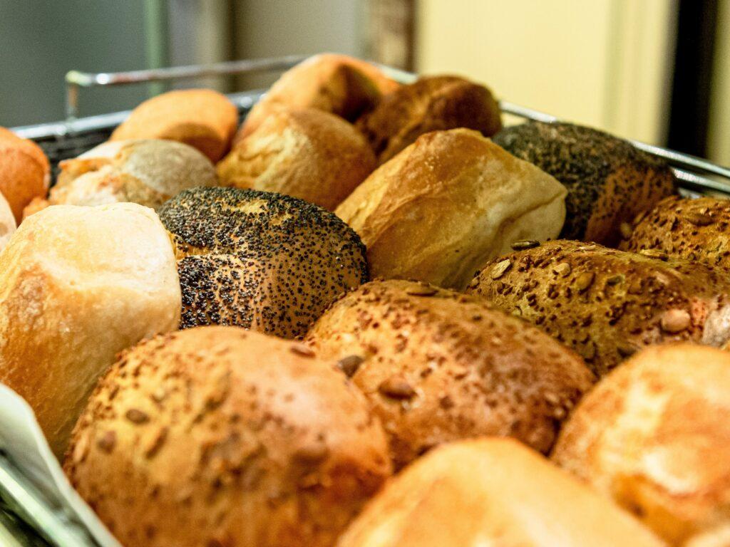 A basket full of freshly baked rolls at the regional breakfast buffet of the sustainable SANDglow hotel in Husum, including grain and wheat rolls that convey warmth and a feeling of fullness in a cozy bakery.