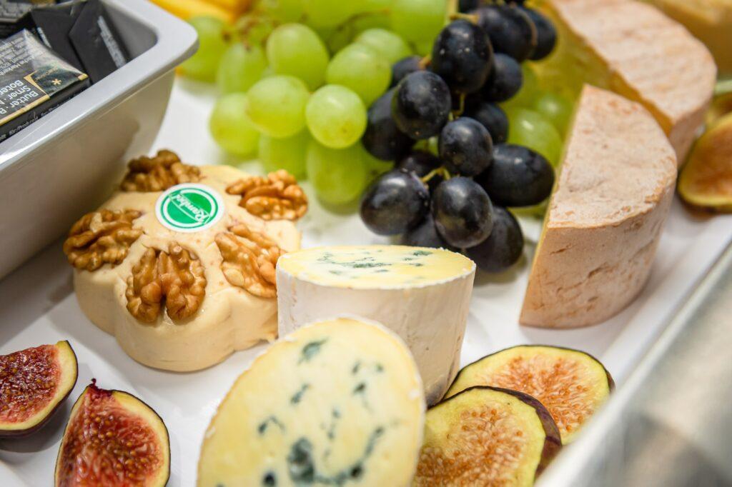 A platter of green and black grapes, sliced figs, round blue cheeses, cheese with walnuts, and slices of bread, creating an elegant, gourmet presentation on the regional breakfast buffet at the sustainable SANDglow Hotel.