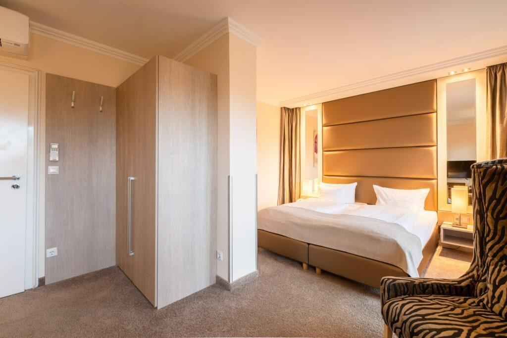 Stylish hotel room at SANDglow, a sustainable boutique hotel on the North Sea coast, with a large bed, beige upholstered headboard, and elegant lighting. The zebra-patterned chair adds a striking accent to the warm interior.