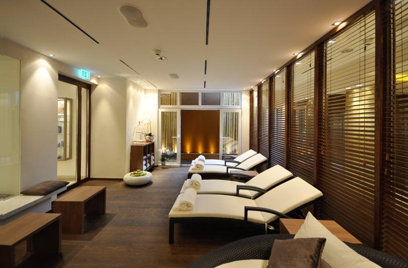 Luxurious spa lounge in the sustainable boutique hotel SANDglow on the North Sea coast, featuring elegant wood décor and white upholstered armchairs. Soft lighting and neatly rolled towels create a calm, relaxed atmosphere.