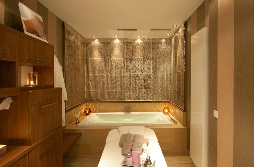 Luxurious spa bathroom with a warm atmosphere; features a large bathtub, elegant wooden cabinets, and a massage table. Relaxed, peaceful atmosphere at the sustainable adults-only SANDglow hotel in Husum.