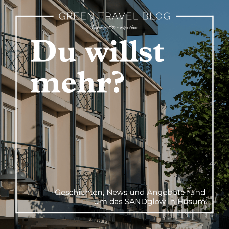 Das moderne Gebäude des nachhaltigen Hotels SANDglow mit Balkonen vor einem strahlend blauen Himmel, umrahmt von Bäumen. Der Text auf dem Bild lautet: „Sie möchten mehr? Geschichten, Neuigkeiten und Angebote von SANDglow in Husum.“ Der Ton ist einladend und informativ.